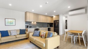 Una sala moderna con un sofá color crema, una mesa de comedor de madera y una cocina con armarios de madera y encimera negra.
