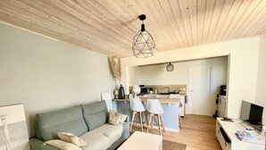 A living room with a sofa, a coffee table, and a TV. There is a kitchen area with a microwave and a sink. - To complete (Pornic)