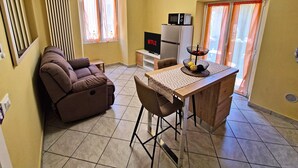 Una sala de estar con sofá, televisor, comedor con mesa y sillas, y zona de cocina con microondas.