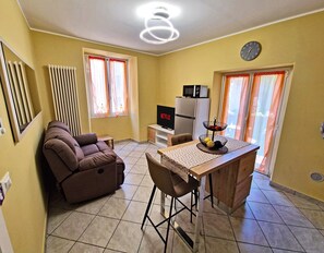 A living room with a sofa, a TV, a dining area with a table and chairs, and a kitchen area with a microwave. - [Romantic Stay - Lake Como - 50m from the lake] (Ossuccio)
