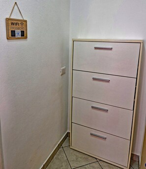 A corner of a room with a white wall, a wooden sign with 'WIFI PASSWORD' and QR code, and a light-colored filing cabinet with three drawers. - [Romantic Stay - Lake Como - 50m from the lake] (Ossuccio)