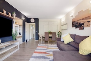 A modern living room with a flat-screen TV, a brown sofa, and a dining area with a table and chairs. - Apartment 'Casa Lanna Medeiros' with Shared Pool, Wi-Fi and Air Conditioning (Albufeira)