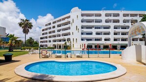 Un hotel amb piscina, diversos balcons i una palmera.