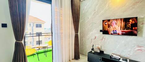 A modern living room with a TV mounted on the wall, a balcony with yellow chairs, and a black entertainment unit.