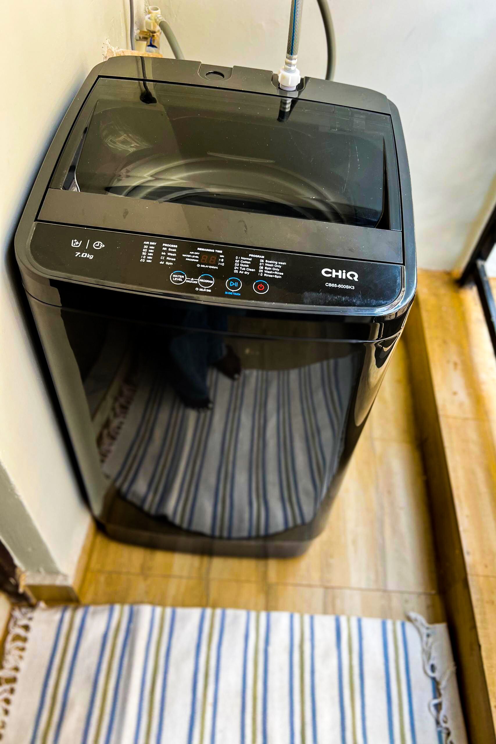 A compact, black, wall-mounted washing machine with a control panel displaying various settings and a water inlet hose.