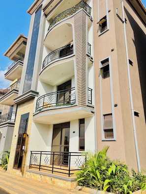 Un edificio residencial de varios pisos con balcones, entrada con portón y camino de acceso pavimentado.