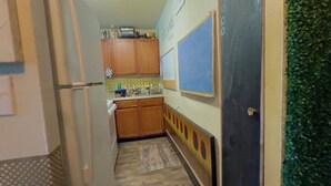 Cocina estrecha con armarios de madera, un refrigerador y una pared azul con una pizarra.