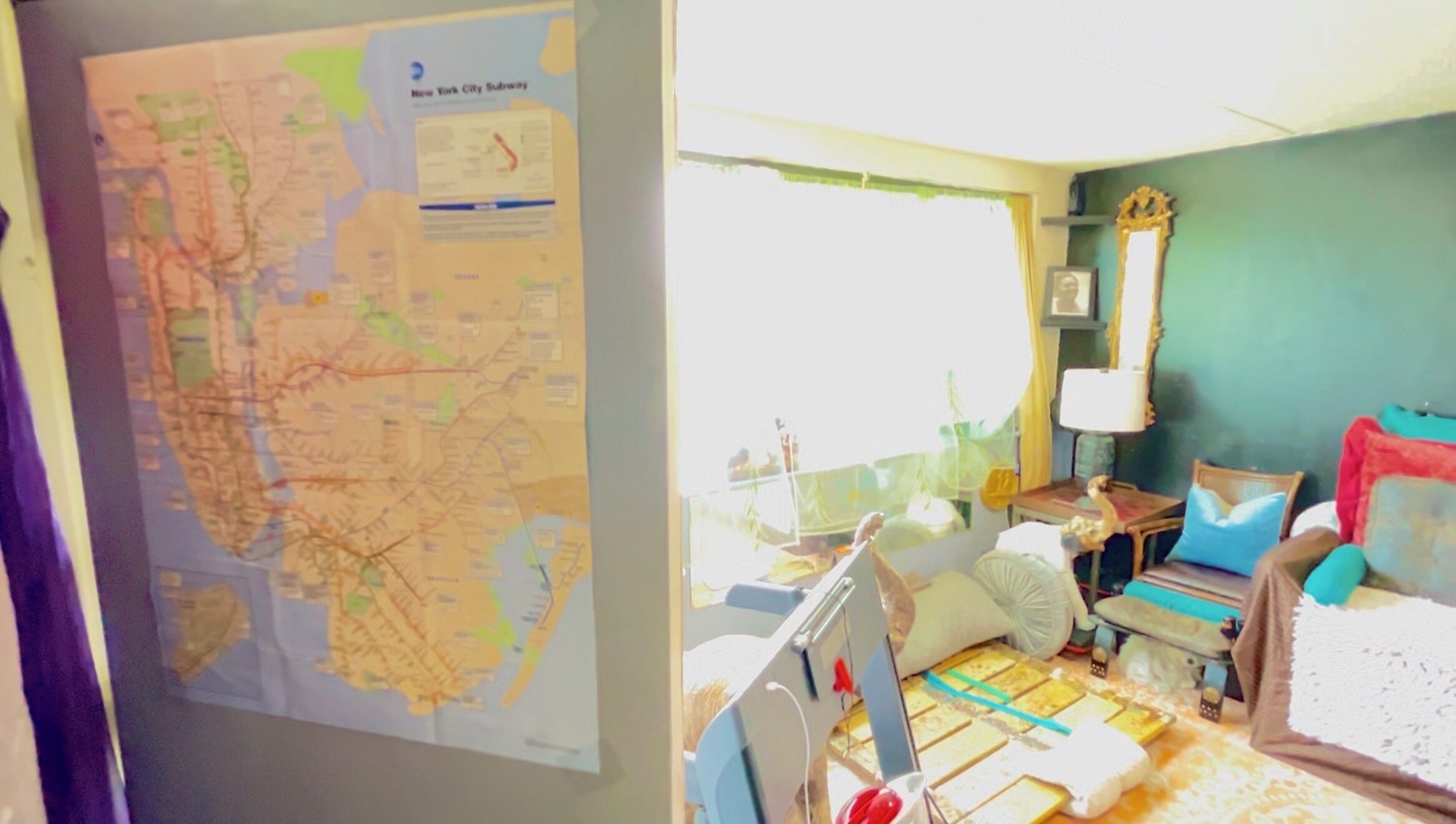 A room with a large map, a bed, a bedside table, a lamp, and a window.