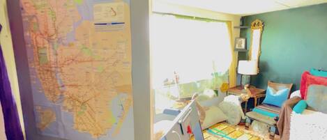 A room with a large map, a bed, a bedside table, a lamp, and a window.