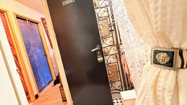 Baño con puerta negra, letrero de 'NO MOLESTAR', una reja metálica decorativa y una cortina blanca.