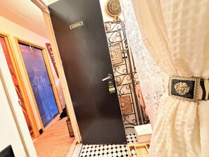 Ein Badezimmer mit einer schwarzen Tür, einem 'DO NOT DISTURB'-Schild, einem dekorativen Metallgitter und einem weißen Vorhang.