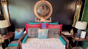Una cama con muchas almohadas, un espejo redondo encima y dos mesitas de noche con lámparas.