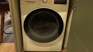 Una lavadora LG compacta e integrada en un apartamento moderno con ventanas amplias y vistas a edificios altos.