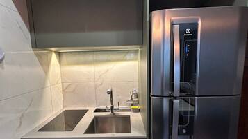 Una cocina compacta con un refrigerador de acero inoxidable integrado, un lavamanos doble y un microondas.