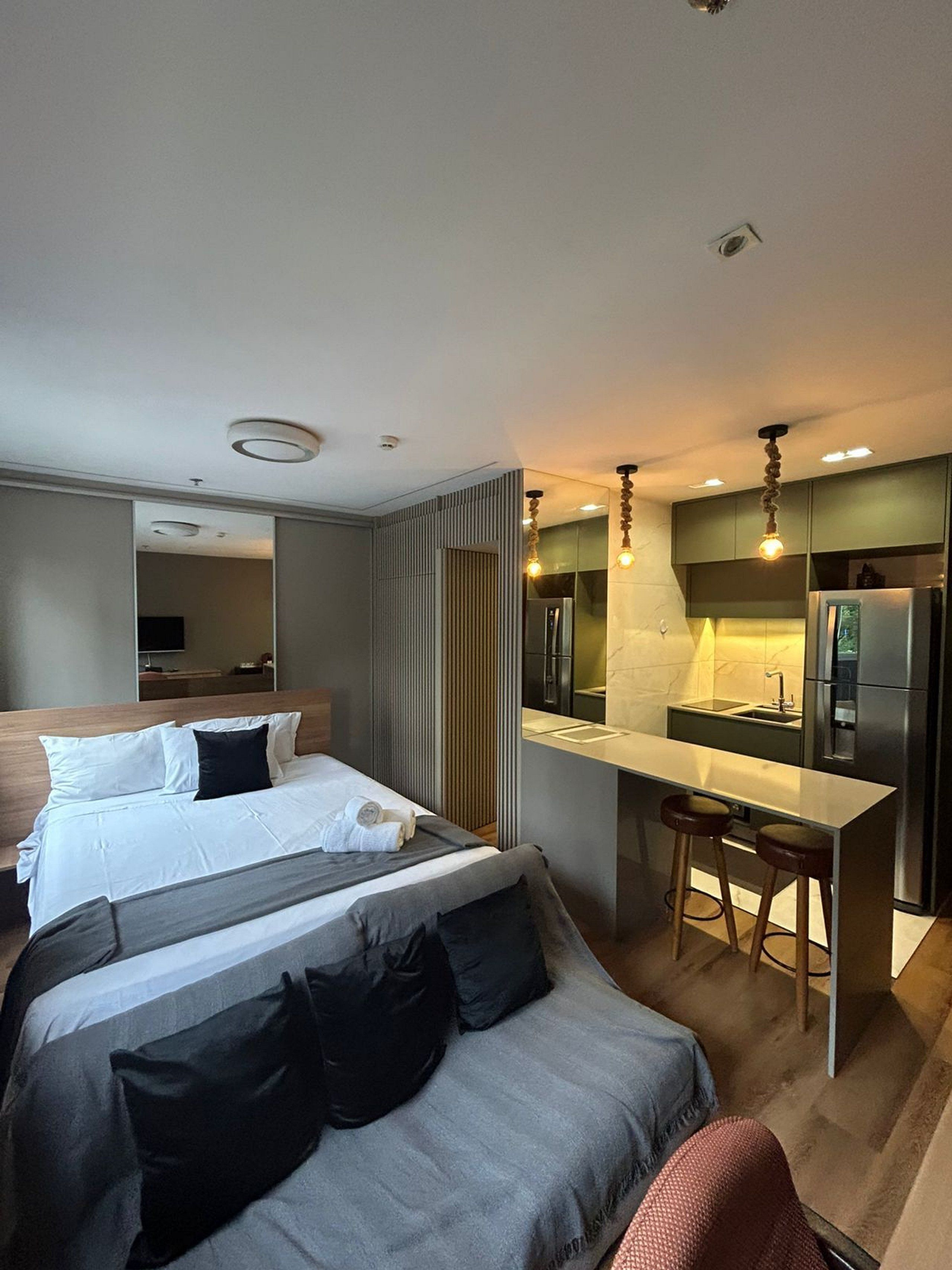 Une chambre d’hôtel moderne équipée d’un lit, d’un canapé, d’un petit coin cuisine avec un réfrigérateur et d’un tabouret de bar.