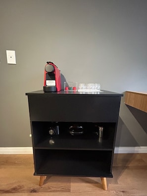 Un módulo de almacenamiento negro con estantes, un electrodoméstico rojo y vasos de vidrio transparentes encima.