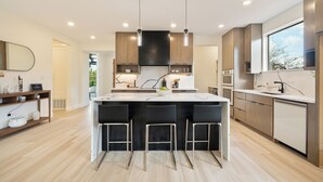 Una cocina moderna con una isla central, taburetes de bar, iluminación colgante y electrodomésticos integrados.