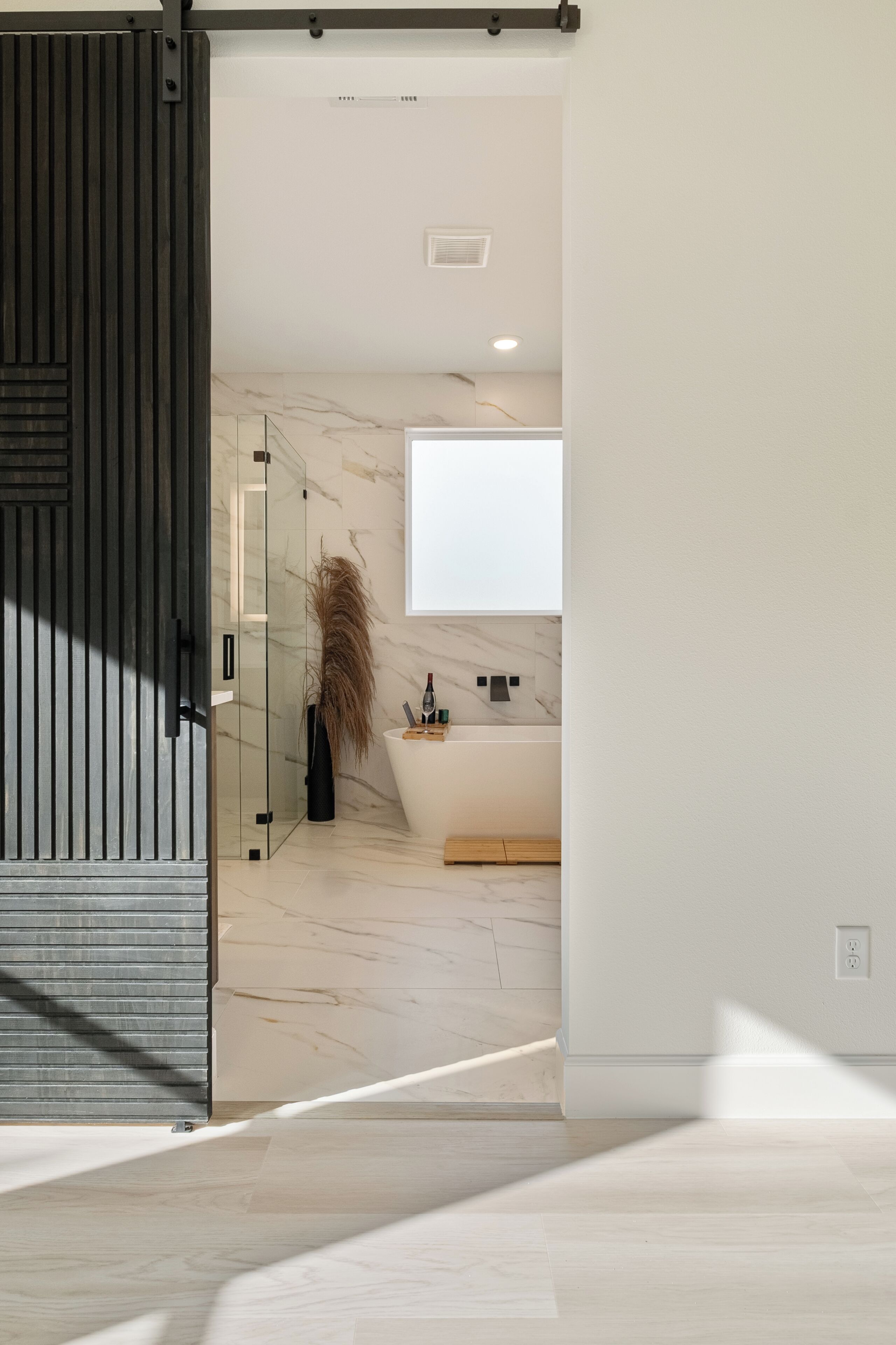 A modern bathroom with a large bathtub, a glass shower enclosure, and a marble wall.