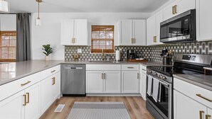 A modern kitchen with white cabinets, stainless steel appliances, and a patterned backsplash.