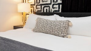 A neatly made bed with patterned pillows, a bedside lamp, and a geometric wall design.