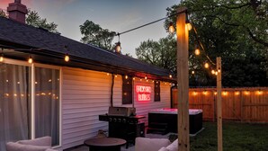 A backyard patio with outdoor furniture, a grill, and string lights.