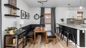 A modern kitchen with a central island, black bar stools, a wooden dining table, and a black leather bench.