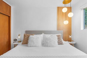 A bedroom with a bed, two bedside tables, a wooden slat wall, and a window.