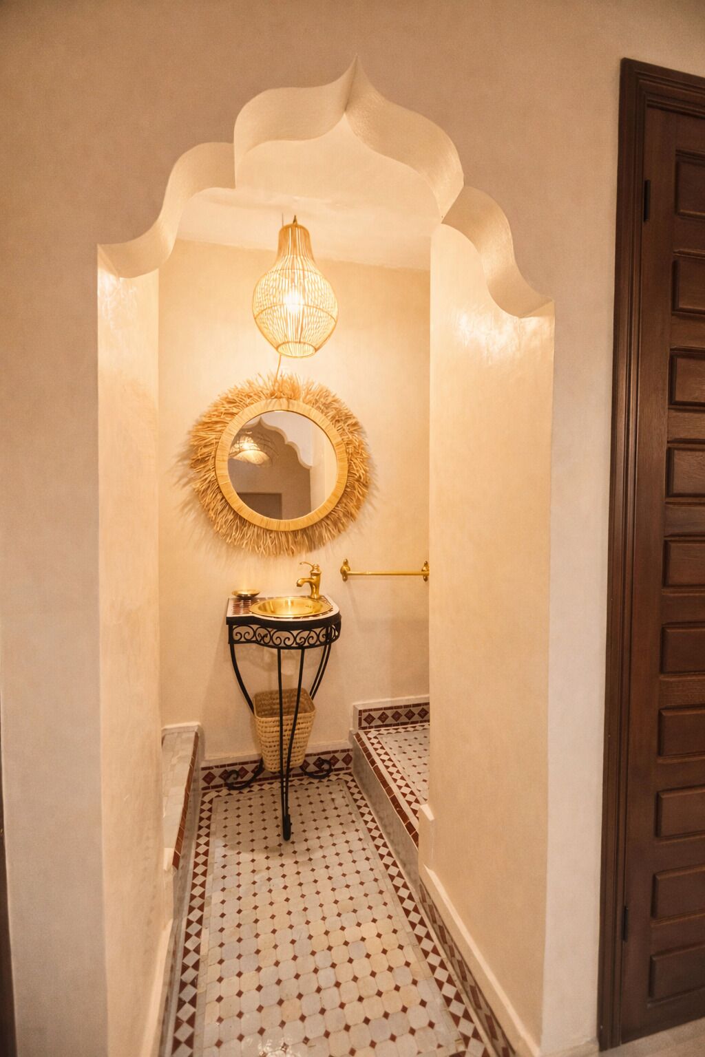 A narrow hallway with a decorative mirror, a gold sink, and a patterned floor.