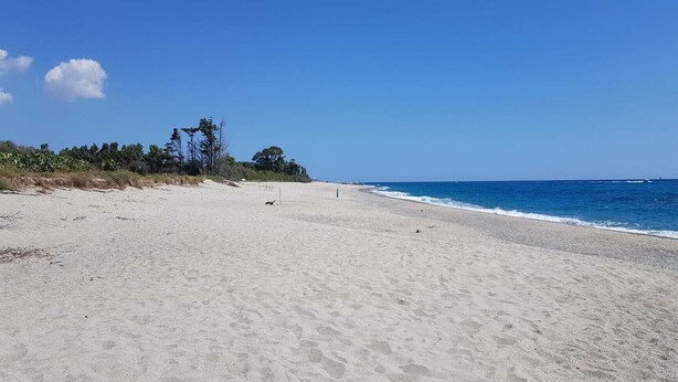 Ein weiter, sandiger Strand mit blauem Himmel und Meer.