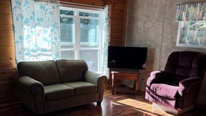 A wooden-paneled room with a sofa, a chair, a television on a wooden stand, and a stone wall.