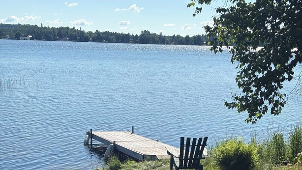 A lakeside view with a dock, two Adirondack chairs, and a bench.