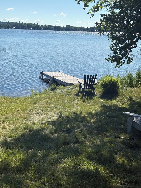 A lakeside view with a dock, two Adirondack chairs, and a bench.