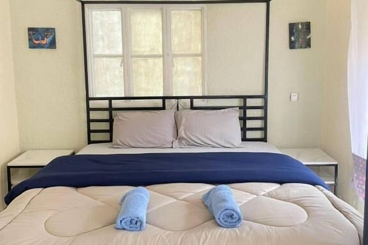 A four-poster bed with a headboard, two pillows, and a blue blanket.