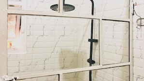 A bathroom with a white marble wall, a black showerhead, and a visible drain. - Saish Stay (Muhoza)