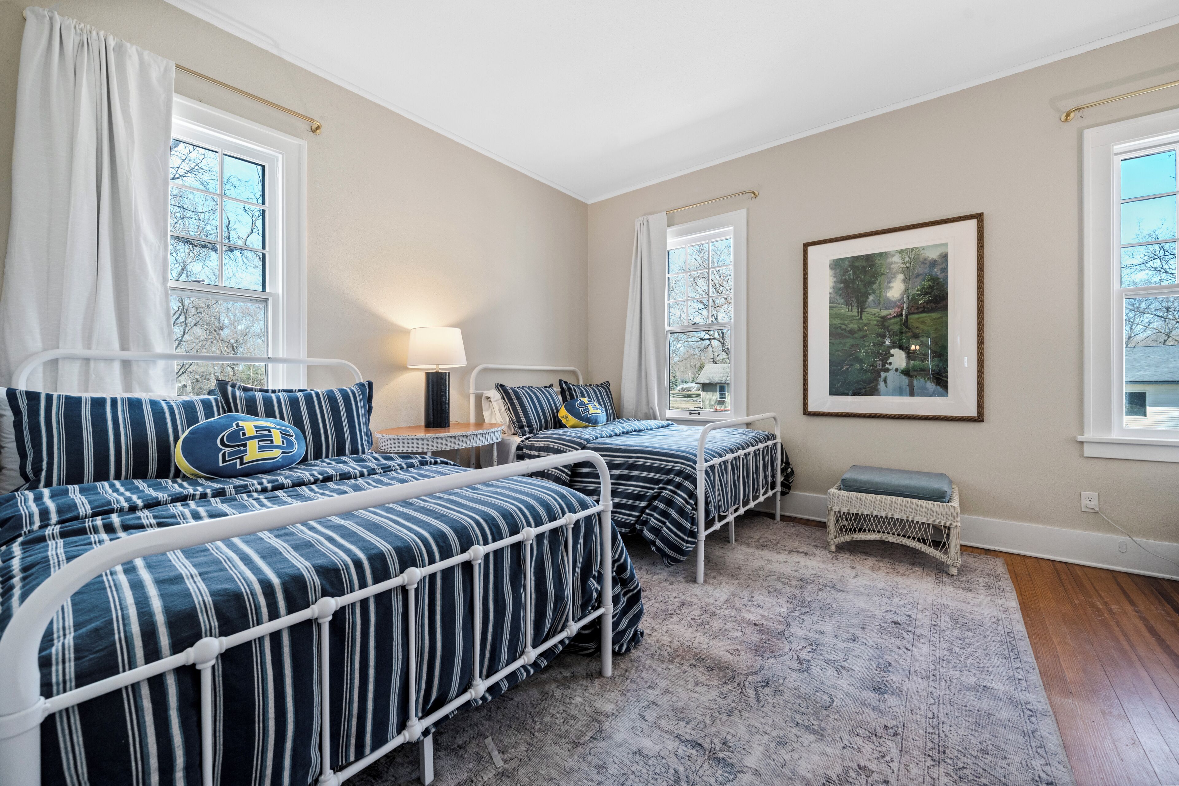 A bedroom with two beds, a bedside table, a lamp, a framed picture, and a window.