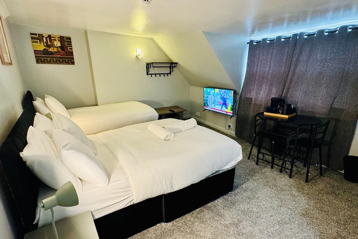 Quarto de hotel com duas camas, uma escrivaninha com cadeira, televisão e uma pequena mesa com cafeteira.