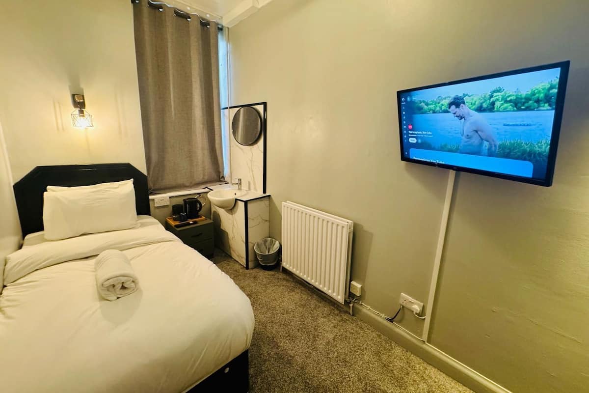 Quarto de hotel com uma cama, mesa de cabeceira com abajur, televisão na parede e janela com cortinas.