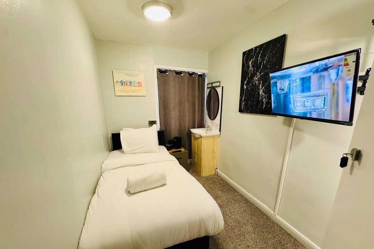Quarto de hotel com cama, televisão na parede, mesa com pia e porta com fechadura.