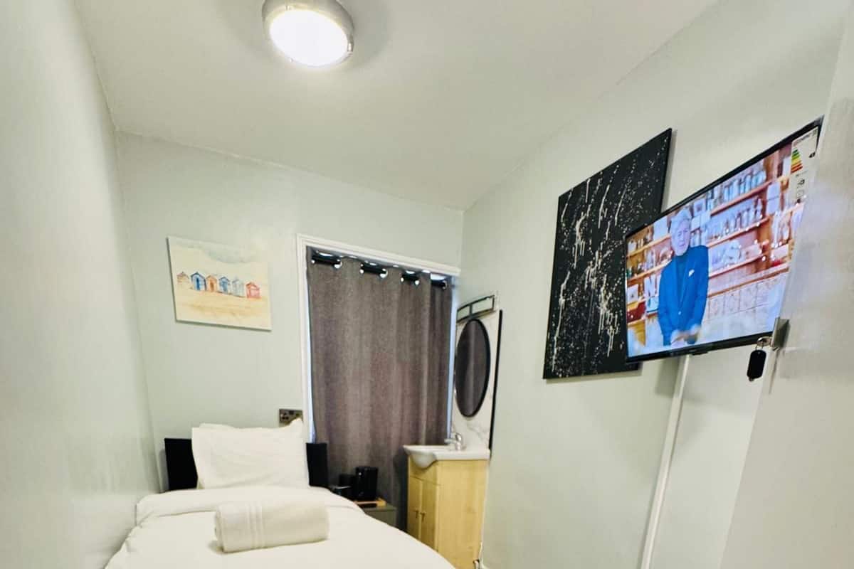 Quarto de hotel com uma cama, televisão presa à parede, um armário pequeno e uma janela com cortinas.