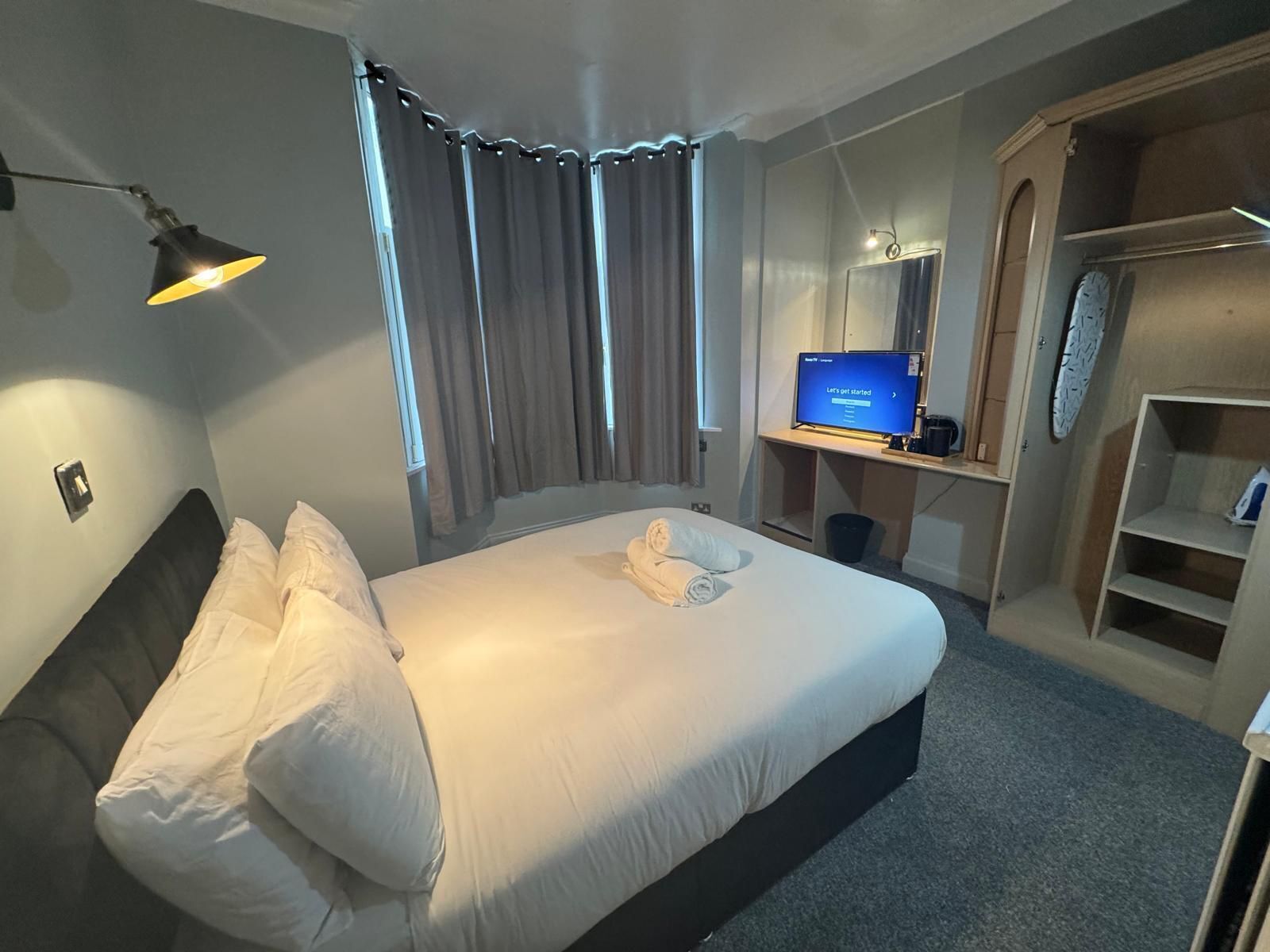 A hotel room with a bed, a desk with a computer, a wardrobe, and a mirror.