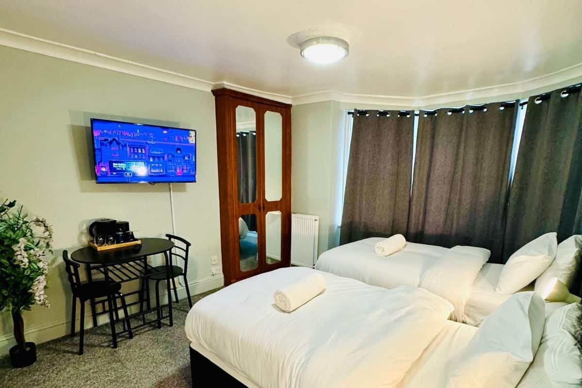 Quarto de hotel com cama, escrivaninha com cadeira, televisão e planta em vaso.