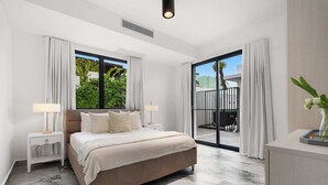 A bedroom with a large bed, two bedside tables, a nightstand, a sliding glass door to a balcony, and a small desk with a vase. - Modern Villa - Private Pool & Rooftop Terrace (San Juan)