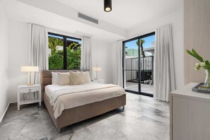 A bedroom with a large bed, two bedside tables, a nightstand, a sliding glass door to a balcony, and a small desk with a vase. - Modern Villa - Private Pool & Rooftop Terrace (San Juan)