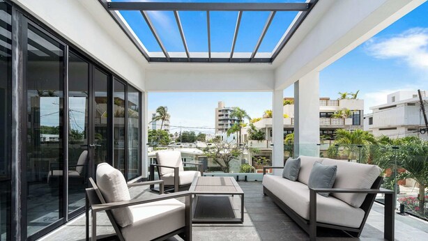 A modern outdoor patio with a glass enclosure, seating, and a view of surrounding buildings. - Modern Villa - Private Pool & Rooftop Terrace (San Juan)