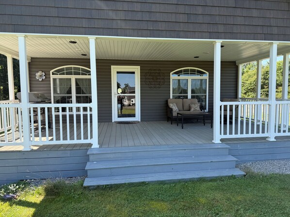A covered porch with a bench and a table, a door, and a small step leading up to the porch.