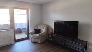 A living room with a beige armchair, a television on a stand, and a sliding glass door leading to a balcony. - Vacation apartment Reinhardt (Nidda)