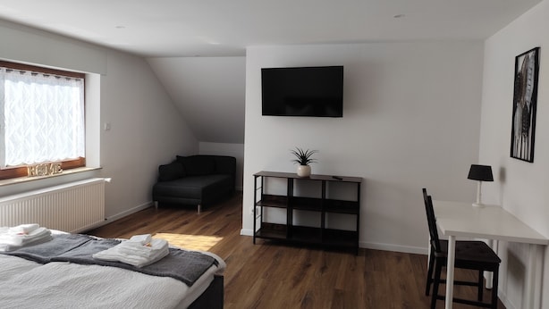 A modern bedroom with a bed, a desk, a chair, a TV, and a window with curtains. - Vacation apartment Reinhardt (Nidda)