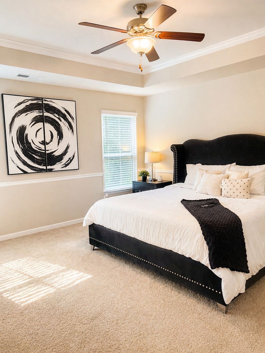 A bedroom with a bed, a ceiling fan, a window with blinds, and a wall art piece.