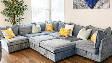 A sectional sofa with multiple cushions, a ceiling fan, a floor lamp, and a painting on the wall.