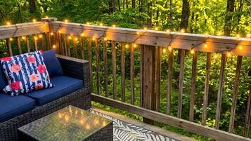 A deck with a sofa and a coffee table, surrounded by a railing with string lights.